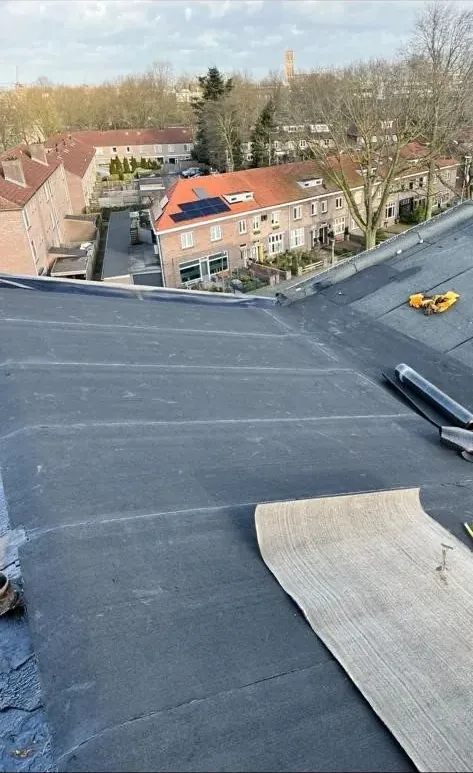 Nieuwe bitumenrol wordt uitgerold op een plat dak boven woningen in Heesch